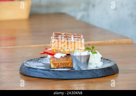 Waffle Strawerry panna fresca nella piastra nera su un tavolo di legno. Foto Stock