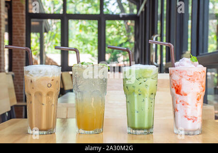 Caffè ghiacciato, miele di Limone , Soda ghiacciata di tè verde e il frullato fragole in vetro sul tavolo di legno sfondo finestre di vetro e l'albero. Foto Stock