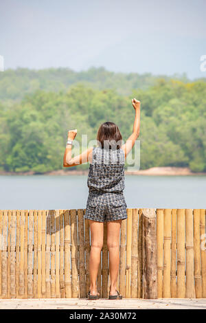 Donne alzando le braccia e sullo sfondo le montagne e acqua al serbatoio Chakrabongse , Prachinburi in Thailandia. Foto Stock