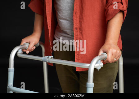 Close-up di giovane donna in piedi e appoggiato sullo scuotipaglia ella cercando di camminare isolati su sfondo nero Foto Stock