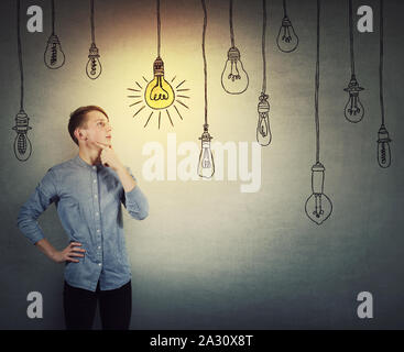 Fiducioso ragazzo adolescente pensare, mantiene una mano sotto il mento pensieroso guardando scegliendo appeso un incandescente lampadina luce da altri sono spenti. L'u Foto Stock