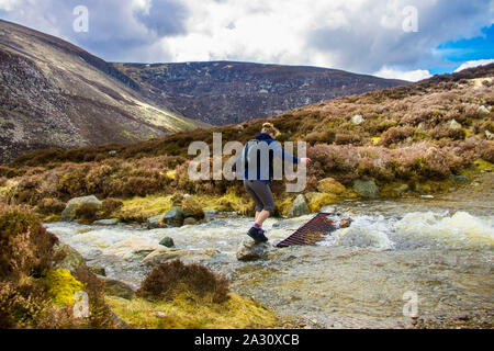 Tourist attraversando il torrente sulla rotta verso il Monte Acuto nel Cairngorm Mountains. Angus, Scotland, Regno Unito Foto Stock