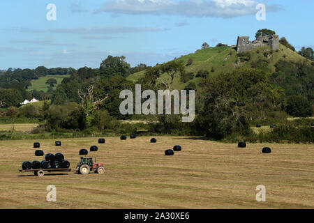 Dryslyn castello situato sulla cima di propria collina ha una posizione dominante sul fiume Towy valley. Un contadino raccoglie nel fieno nei campi sottostanti. Foto Stock