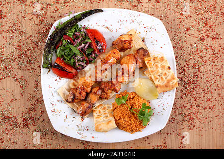 Spiedini di pollo che serve di pollo con sugo di carne e verdure fresche sulla piastra bianca sul tavolo pieno di elevato angolo di spezie piccanti Foto Stock