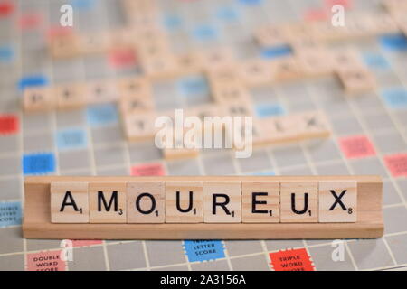 La parola francese 'amoureux' (in inglese: "nell'amore") in legno piastrelle scrabble su un rack. Sullo sfondo di una scheda vintage, fuori fuoco con spazio di copia Foto Stock