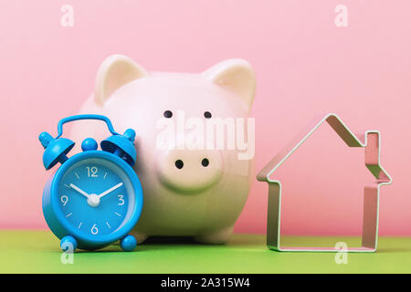 Il suo tempo per salvare fino per immobili. Sveglia, salvadanaio e oggetto nella forma di una casa. Concetto di accumulare denaro per alloggiamento Foto Stock