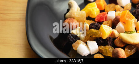 Tutti frutti. Mix di frutta secca (uva passa, cedro, mango) e dadi (mandorle, nocciole) su un nero laccato piatto Foto Stock