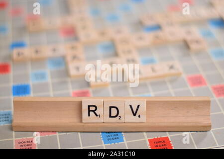 La parola francese "rdv" (in inglese: 'date') in legno piastrelle scrabble su un rack. Sullo sfondo di una scheda vintage, fuori fuoco con spazio di copia Foto Stock