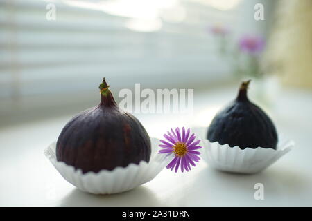 Due mature sweet fichi in carta marrone e un crisantemo fiore su un davanzale bianco. Messa a fuoco selettiva. Foto Stock