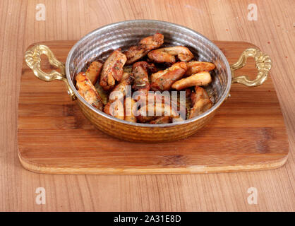 Servizio di pollo fritto in olio animale in un vaso di rame da un angolo stretto su un tavolo di legno Foto Stock