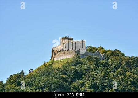 Kapusan rovine del castello, sulla cima di una montagna boscosa, con un flag su una torre contro un cielo blu chiaro in Slovacchia, vicino alla città di Presov. Foto Stock