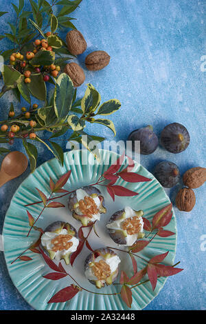 Vista dall'alto. Piastra di colore verde con fichi freschi ripieni di crema di formaggio e dadi. Decorazione di foglie e i dadi su sfondo blu. Foto Stock