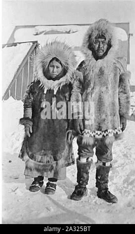 Eschimese giovane indossare pellicce eskimo e mukluks in piedi nella neve con edifici in background posizione sconosciuta ca 1899 Foto Stock