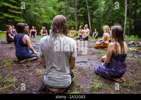 Un giovane ragazzo boemo con lunghi capelli biondi che indossa un imbevuto di t-shirt è visto in ginocchio in un cerchio con la gente in cerca di illuminazione e guida spirituale. Foto Stock