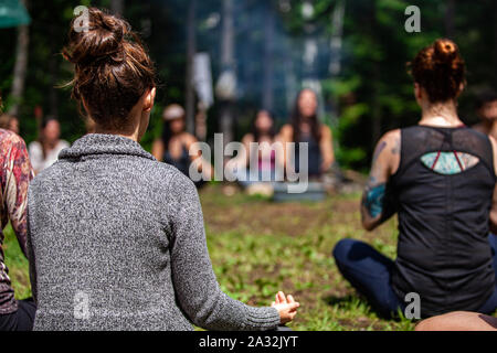Un open minded gruppo di individui misti sono visto seduti intorno a un campeggio in profonda meditazione in cerca di consapevolezza e di illuminazione. Foto Stock