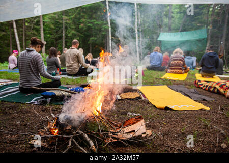 Una vista ravvicinata di fiamme che si erge da un fuoco di campo come sfocata si vedono persone in cerca di illuminazione e consapevolezza durante la meditazione di gruppo. Foto Stock