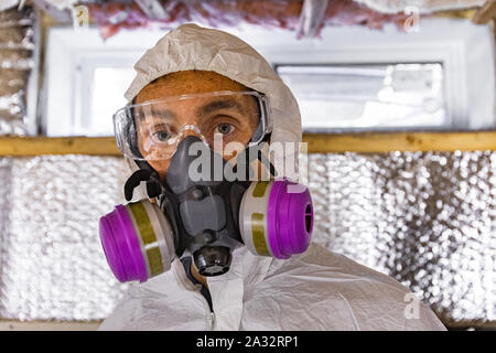 Una vista ravvicinata di un edificio caucasica assessore Indossare respiratore professionale & eye occhiali protettivi durante un'ispezione delle pareti di un edificio, con isolamento dietro. Foto Stock