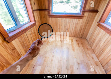 Una vista ingrandita di un uomo utilizzando una lente di ingrandimento all'interno di una abitazione domestica camera con pavimento in legno e muri rivestiti durante la piscina home ispezione con copy-spazio. Foto Stock