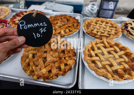 Un prezzo francese tag, dicendo le mele, è visto da vicino nella mano di un fornaio per la vendita di frutta e rabboccato pasticceria torte dolci su uno stallo durante un mercato agricolo. Foto Stock