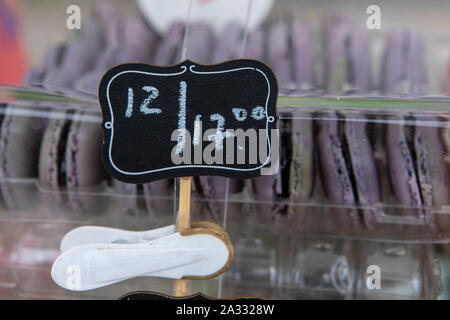 Un primo piano di un piccolo segno di prezzo da un display stand di pane appena sfornato amaretti francese (macarons), venduto su un panificio in stallo durante un mercato agricolo. Foto Stock