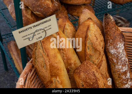 Pane appena sfornato baguette sono visti closeup, visualizzati in un cesto di vimini su uno stallo presso un mercato agricolo, con il francese canadese prezzo sull'etichetta. Foto Stock