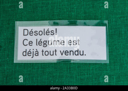 Un piccolo segno francese dicendo siamo spiacenti, questo vegetale è già venduti, è visto primo piano su un mercato in stallo con venduti fuori produzione, contro uno sfondo verde. Foto Stock
