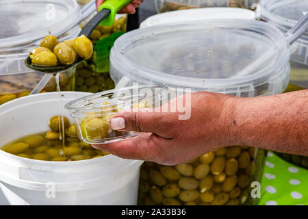 Un primo piano sulle mani di una persona, la scelta di olive organici da contenitori di grandi dimensioni su un mercato in stallo durante un locale fiera agricola. Foto Stock