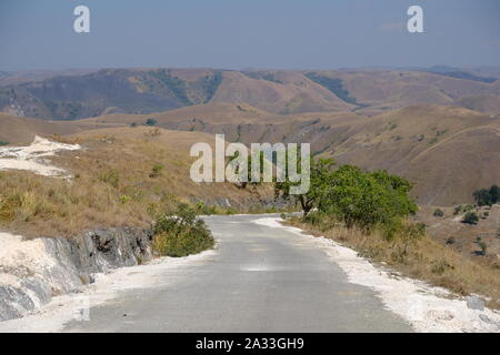 Indonesia Isola di Sumba vista orizzontale di una solitaria strada di campagna e colline Foto Stock