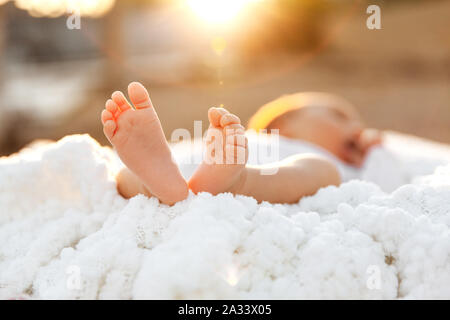 Piede neonato sulla soffice coltre bianca al tramonto in un fuoco selettivo closeup dei piedi nudi - Immagine Foto Stock