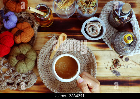 Top vista donna mano tenere tazza di caffè del mattino su sfondo autunno con decorazione stagionale tavolo ornamento per la casa decorazione come zucca, tela di piatto burlap Foto Stock