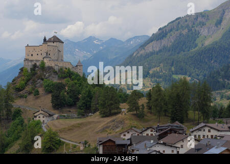 Piccolo villaggio di montagna e un castello sulla sommità di un colle naturale al giorno nuvoloso con swiss panorama di montagna in background. Foto Stock