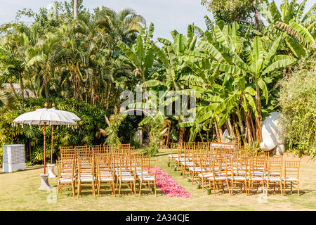 Round arco di matrimonio in stile Boho per una cerimonia decorata con vegetazione fresca e fiori. Tiffany sedie e rosa e rosso petalo corsia. Foto Stock