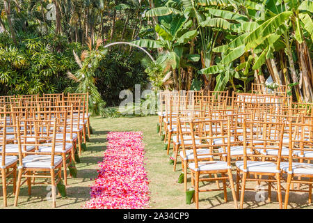 Round arco di matrimonio in stile Boho per una cerimonia decorata con vegetazione fresca e fiori. Tiffany sedie e rosa e rosso petalo corsia. Foto Stock