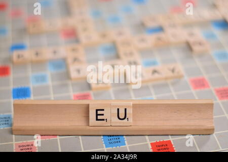 Il nome "UE" (Unione Europea) in legno piastrelle scrabble su un rack. Lo sfondo è una scheda vintage, fuori fuoco con copia spazio. Foto Stock