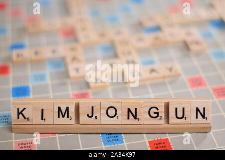 Il nome 'KIM JONG ONU" (il capo supremo della Corea del Nord) in legno piastrelle scrabble su un rack. Lo sfondo è una scheda vintage, fuori fuoco, spazio di copia Foto Stock