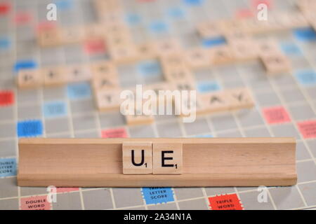 La parola "UE" (Union Européenne o Unione europea) in legno piastrelle scrabble su un rack. Lo sfondo è una scheda vintage, fuori fuoco con copia spazio. Foto Stock