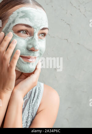 Ritratto di una donna felice facendo maschera facciale di una argilla blu, con il piacere di toccare il viso con le mani, coccole e trattamenti di bellezza concetto Foto Stock