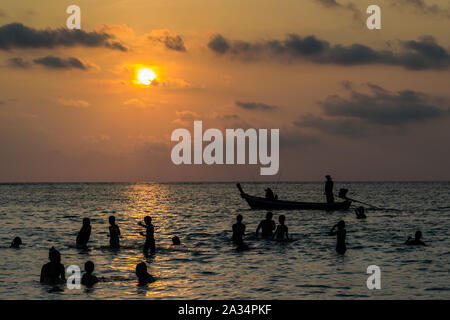 Stagliano gruppo di persone stanno giocando in mare con una barca dalla coda lunga durante il tramonto Foto Stock