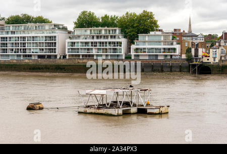 Un piccolo arrugginito molo galleggiante nelle acque sporche del fiume Tamigi di fronte case residenziali sulle rive, Londra, Inghilterra Foto Stock