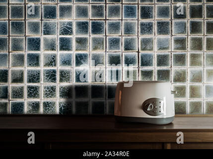 Tostapane bianco sulla credenza in legno nella camera da cucina con piastrelle vintage parete contro la luce calda Foto Stock