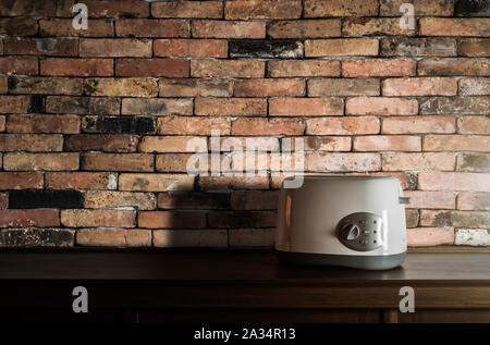Tostapane bianco sulla credenza in legno in cucina con camera vintage muro di mattoni contro luce calda Foto Stock