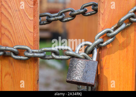 Catena di acciaio con un lucchetto sul gate di un luminoso recinzione di legno Foto Stock