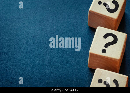 Bordo laterale dei punti interrogativi su cubi di legno su un blu scuro dello sfondo testurizzata con spazio di copia Foto Stock