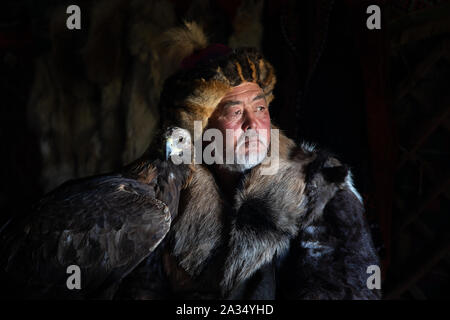 Close up ritratto di un vecchio kazako cacciatore di EAGLE con la sua maestosa aquila reale in ambienti interni in dark tradizionali ger kazake. Ulgii, Mongolia occidentale. Foto Stock