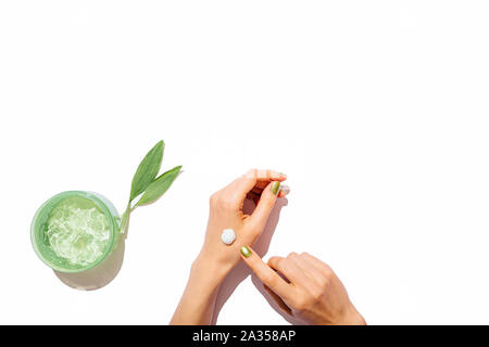 Vista superiore della donna si applicano le mani crema cosmetica accanto al gel di aloe e foglie verdi su sfondo bianco, disposizione piatta. Foto Stock