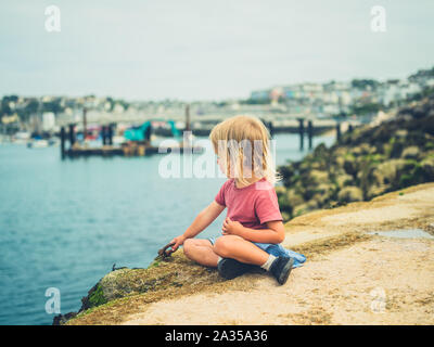 Un piccolo bambino è seduto nel porto in un giorno di estate Foto Stock