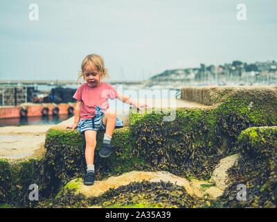 Un piccolo bambino è seduto nel porto in un giorno di estate Foto Stock