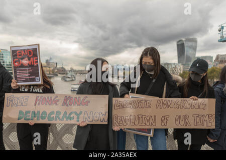 Londra, Regno Unito. 5 Ottobre, 2019. Artista cinese Badiucao sostenitori e unire le mani in una catena umana, una mostra di solidarietà con i dimostranti di Hong Kong. Il muro di Lennon bandiera, simboleggia la Hong Kongs lotta per la libertà è anche simbolicamente sollevata. Penelope Barritt/Alamy Live News Foto Stock