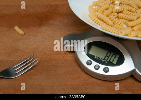 80 grammi di pasta in un piatto di una bilancia da cucina su un tagliere di legno Foto Stock
