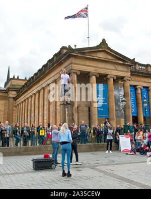 Street performer e giocoliere equilibratura su palo. Al di fuori della Scottish National Gallery di Edimburgo. Foto Stock